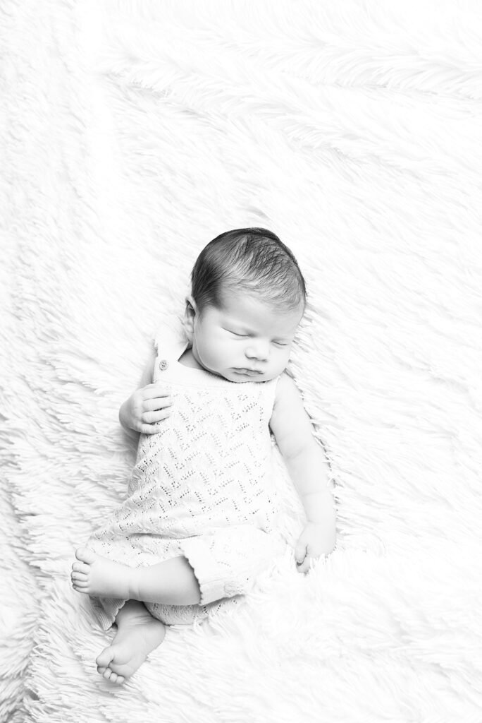 Black and white photo of a newborn baby sleeping peacefully on a textured blanket.